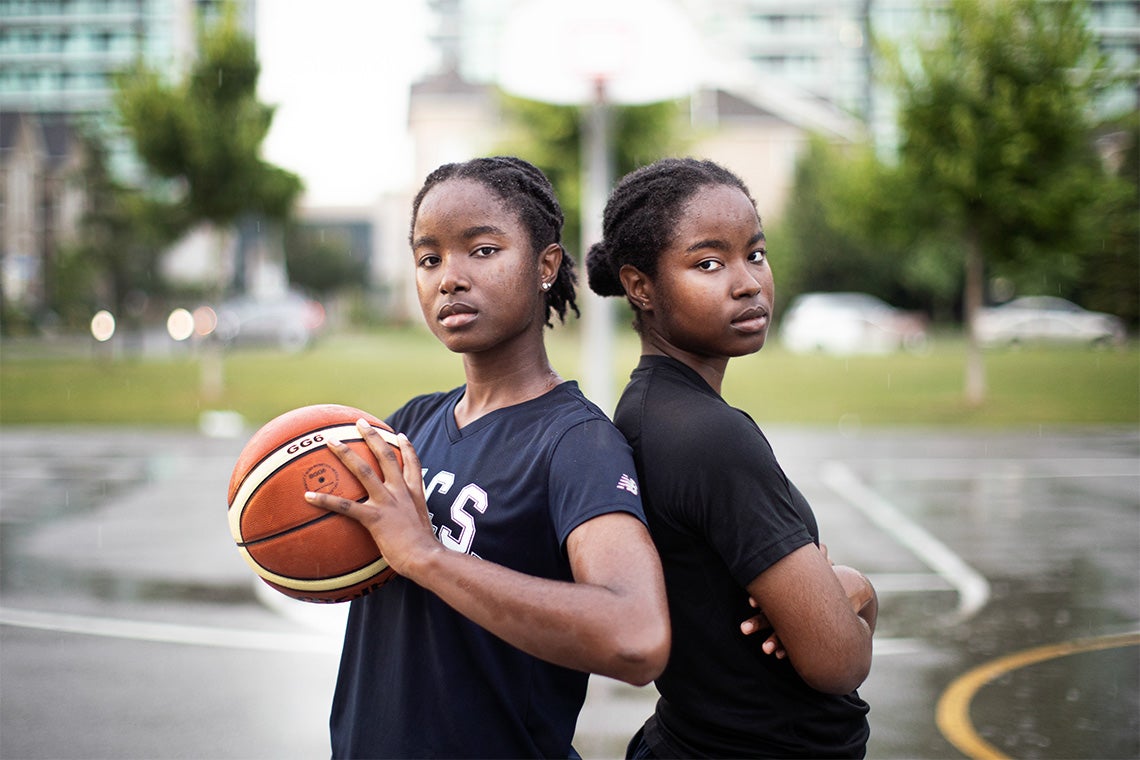 Mikhaela and Nakeisha Ekwandja pose on a rainy downtown basketball court
