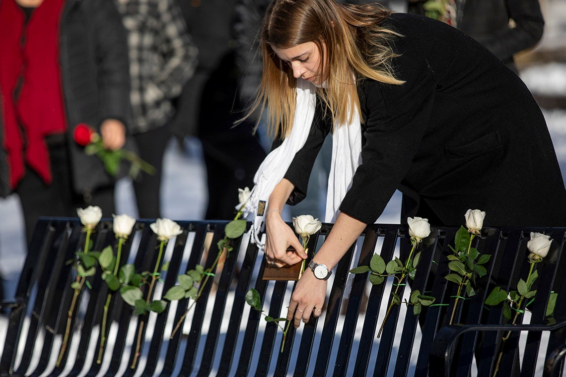 A woman weaves roses into the memorial bench at U of T on the National Day of Remembrance