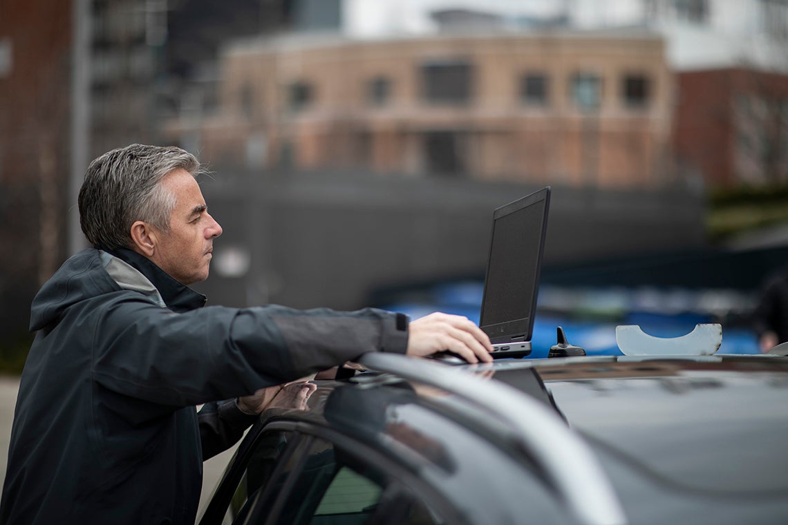 Nicholas Hoban uses a laptop on top of his car