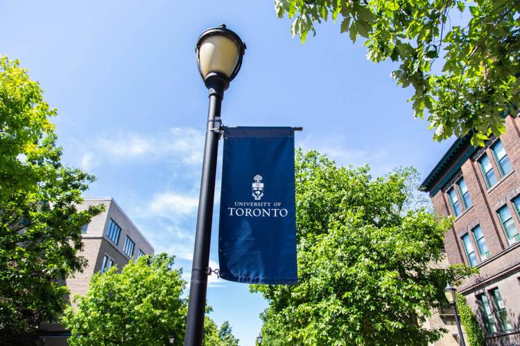 A U of T banner hangs from a lamp post on campus