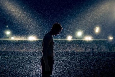 silhouetted athlete looks down at his feet in a darkened stadium