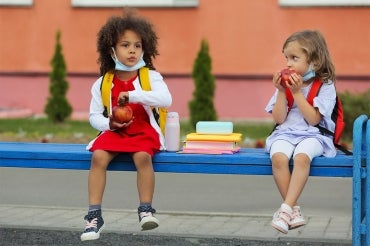 two young children sit outside to eat their lunch