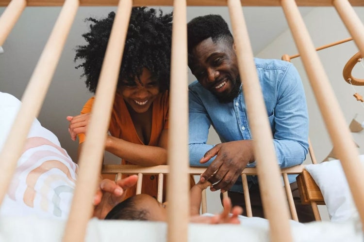 a mother and father interact with their child in a crib