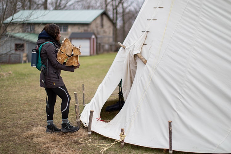 A woman carries wood into a teepee