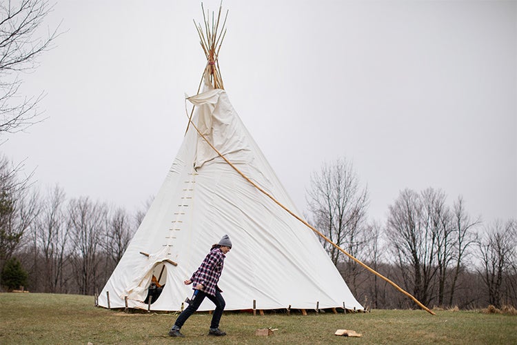 a woman walks past a teepee on a grey fall afternoon