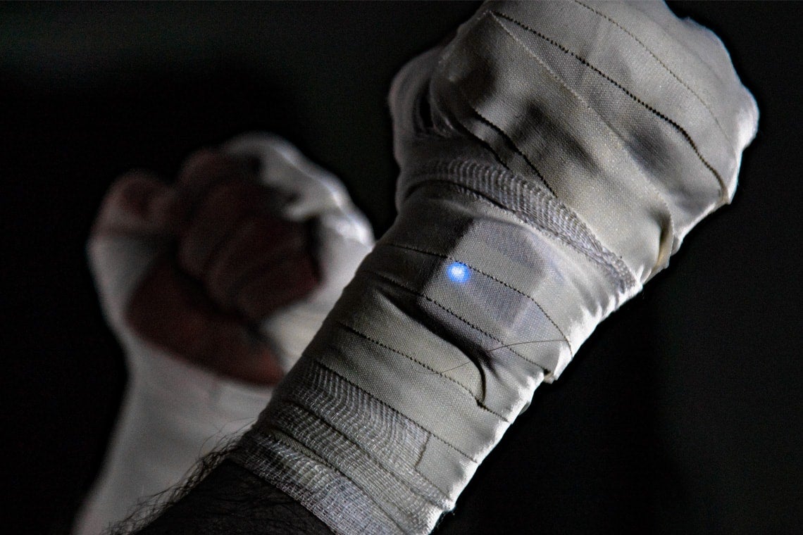 Photo of hands bandaged in fighting ready stance with wrist-mounted sensor 
