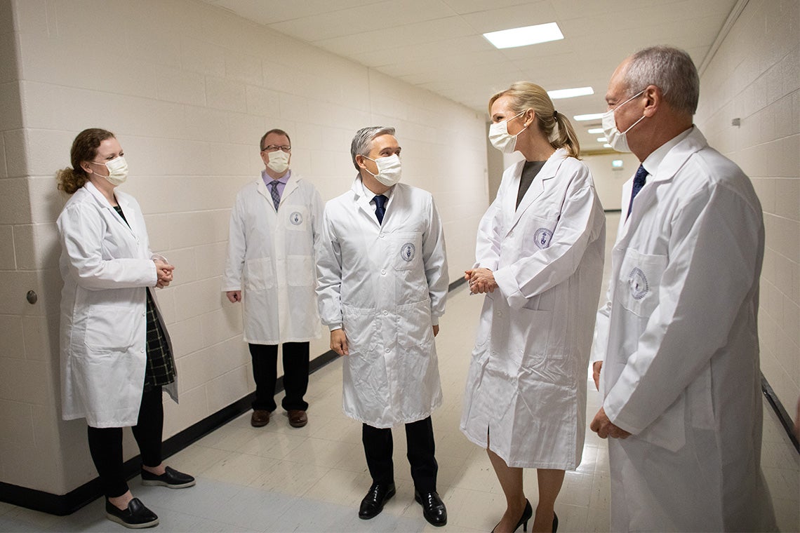 François-Philippe Champagne chats in a hallway with U of T faculty. Everyone wears protective masks and lab coats.