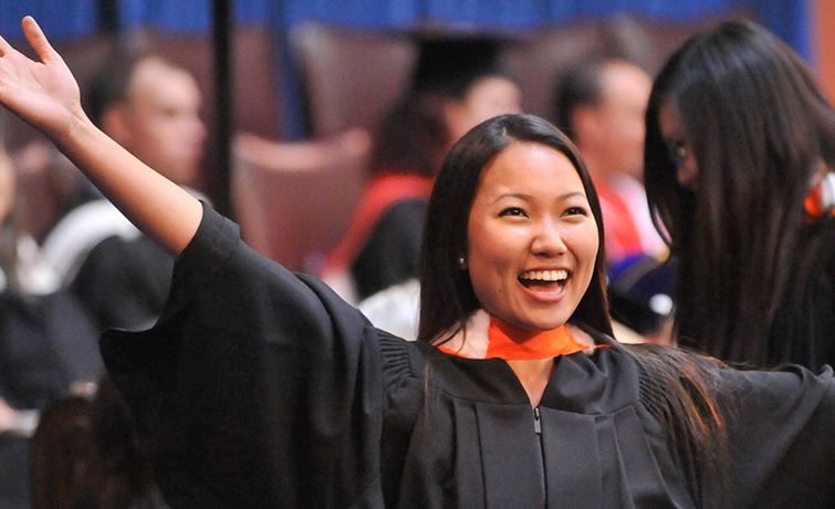 A graduate in regalia raises her arms in celebration during convocation.