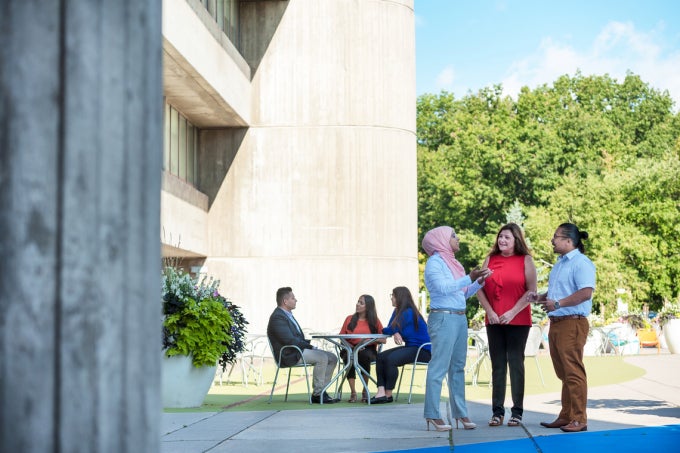 Three people conversing, while three more sit at a table in the background on the UTSC campus.