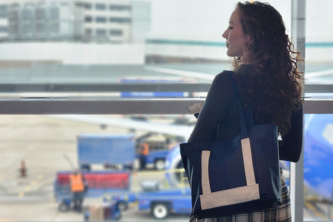 woman standing by a window at the airport carrying an upcycled leather bag made from airplane seats