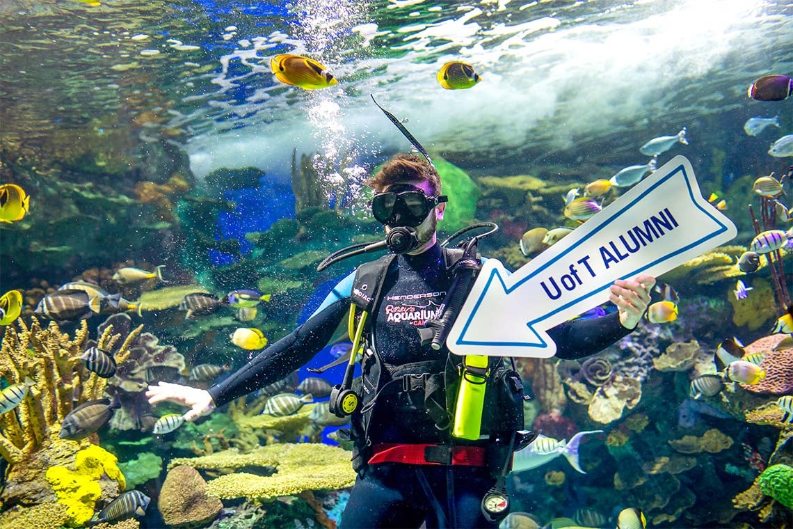 Scuba diver in the Ripely's Aquarium fish tank holding a U of T Alumni arrow directing guests to the party