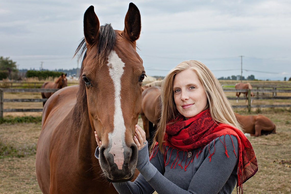 Carolyn Creed poses outside with a brown and white horse