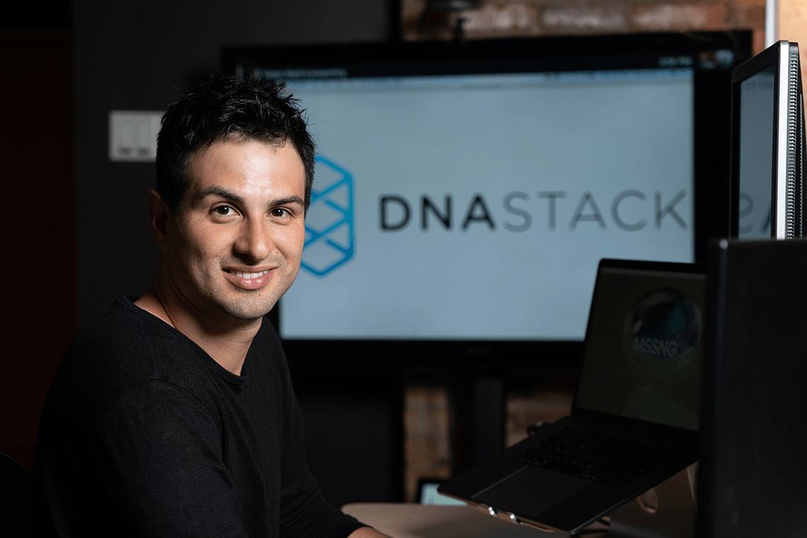 Marc Fiume sits in front of computer monitors displaying the logo of his genomics software startup, DNAstack.