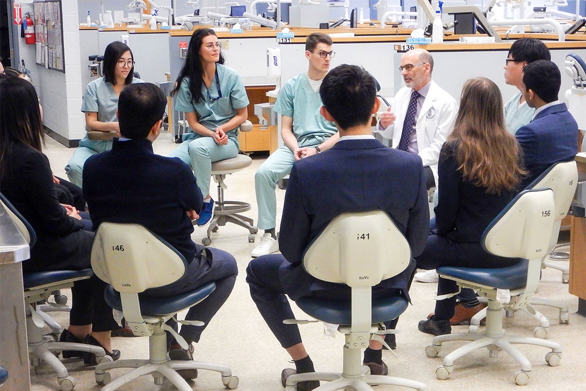 a group of students seated in chairs in  a dentistry classroom surround dean Daniel Haas