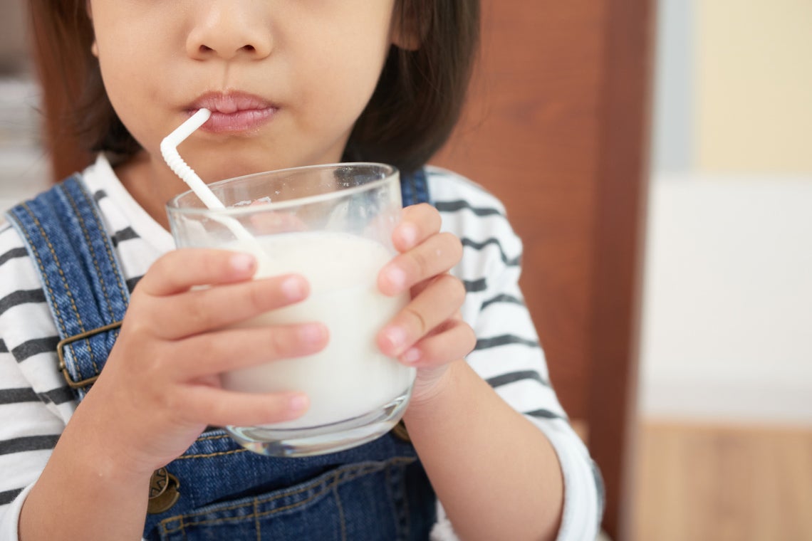 an anonymous young girl is drinking a glass of milk through a straw