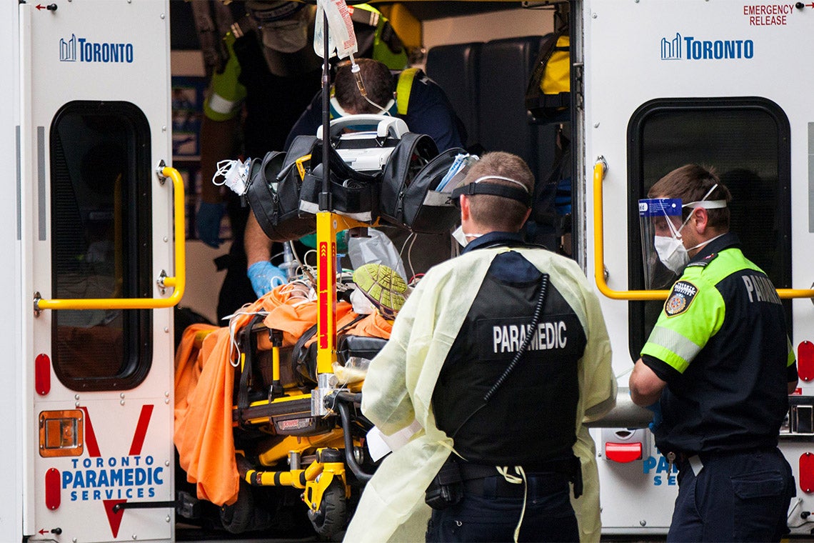 Toronto paramedics dressed in PPE take a patient out of an ambulance