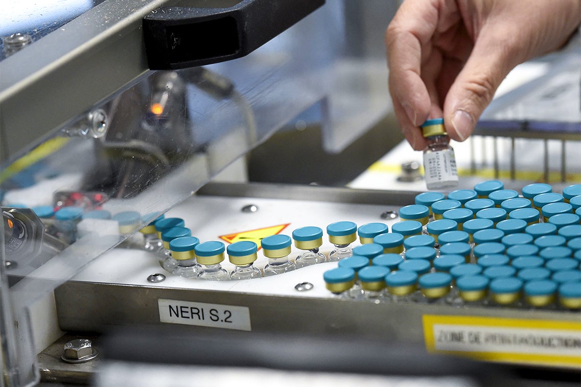 a hand pulls out a vial of covid-19 vaccine from a production line at a glaxo-smith kline facility in France