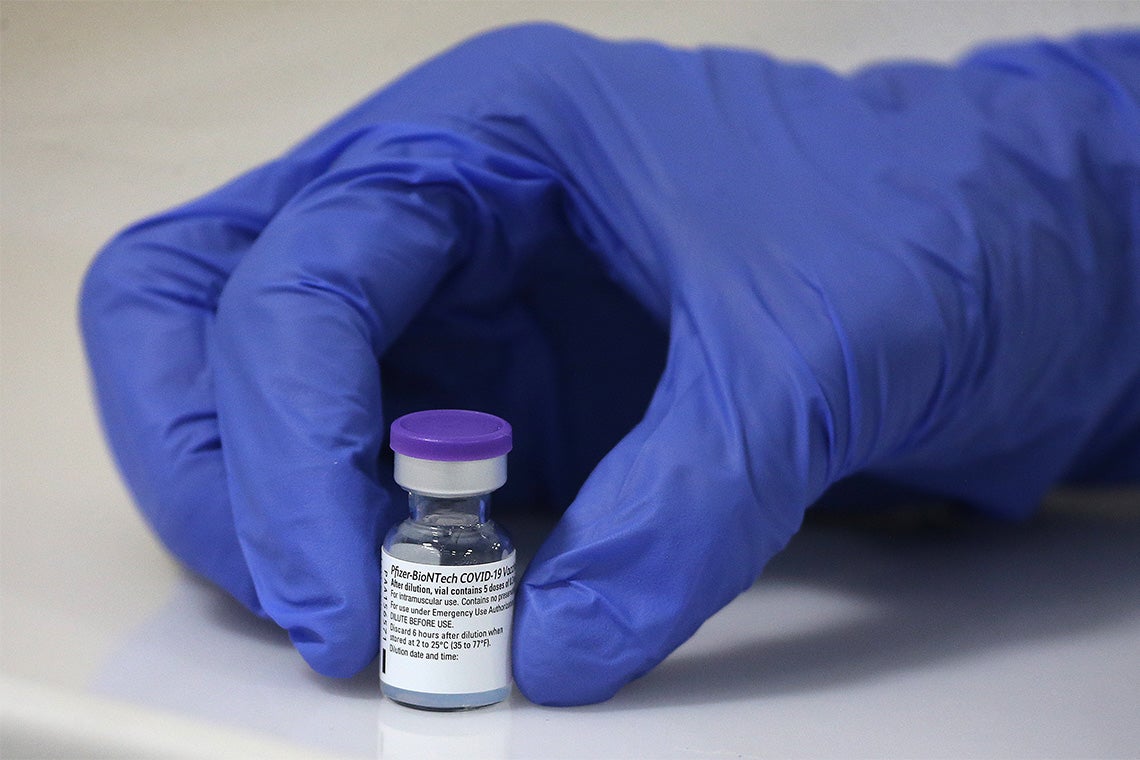 A gloved hand holds a vial of pfizer covid vaccine