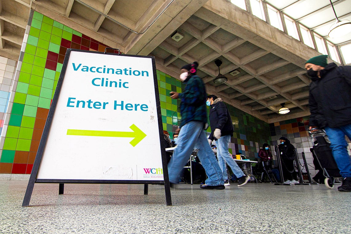 people walk past a sign that reads "vaccination clinic enter here"