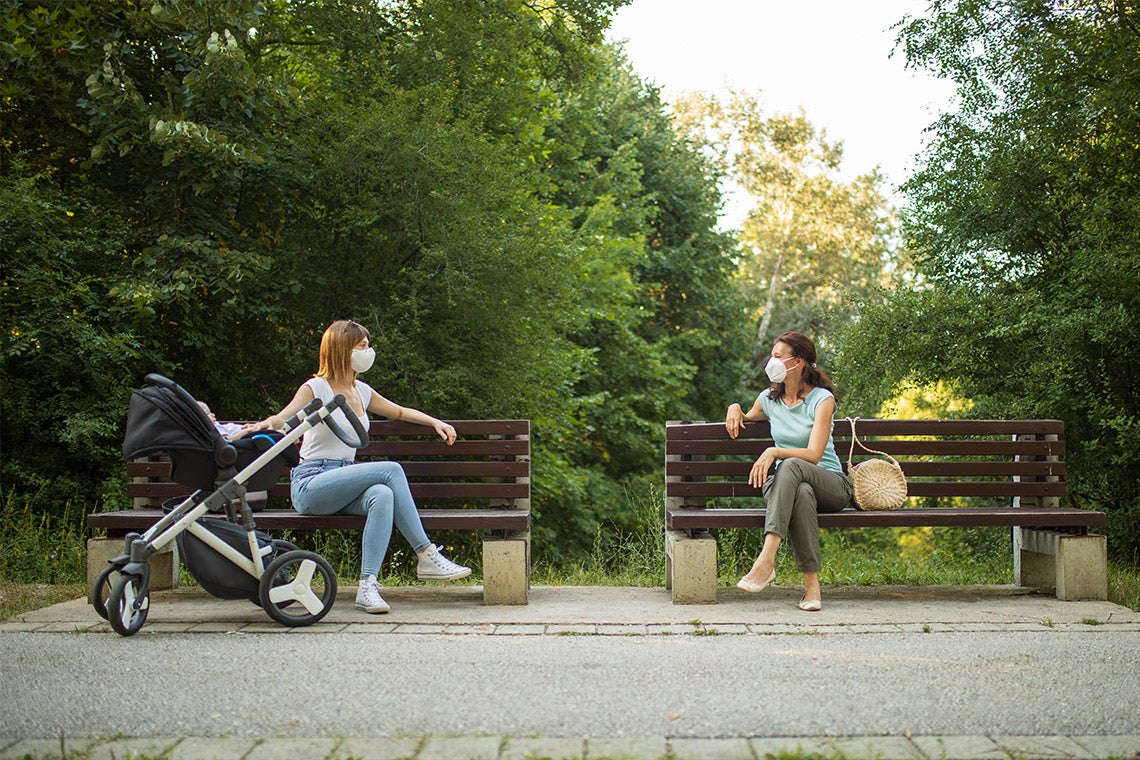 Two women, socially distanced, having a conversation in a park with surgical masks on