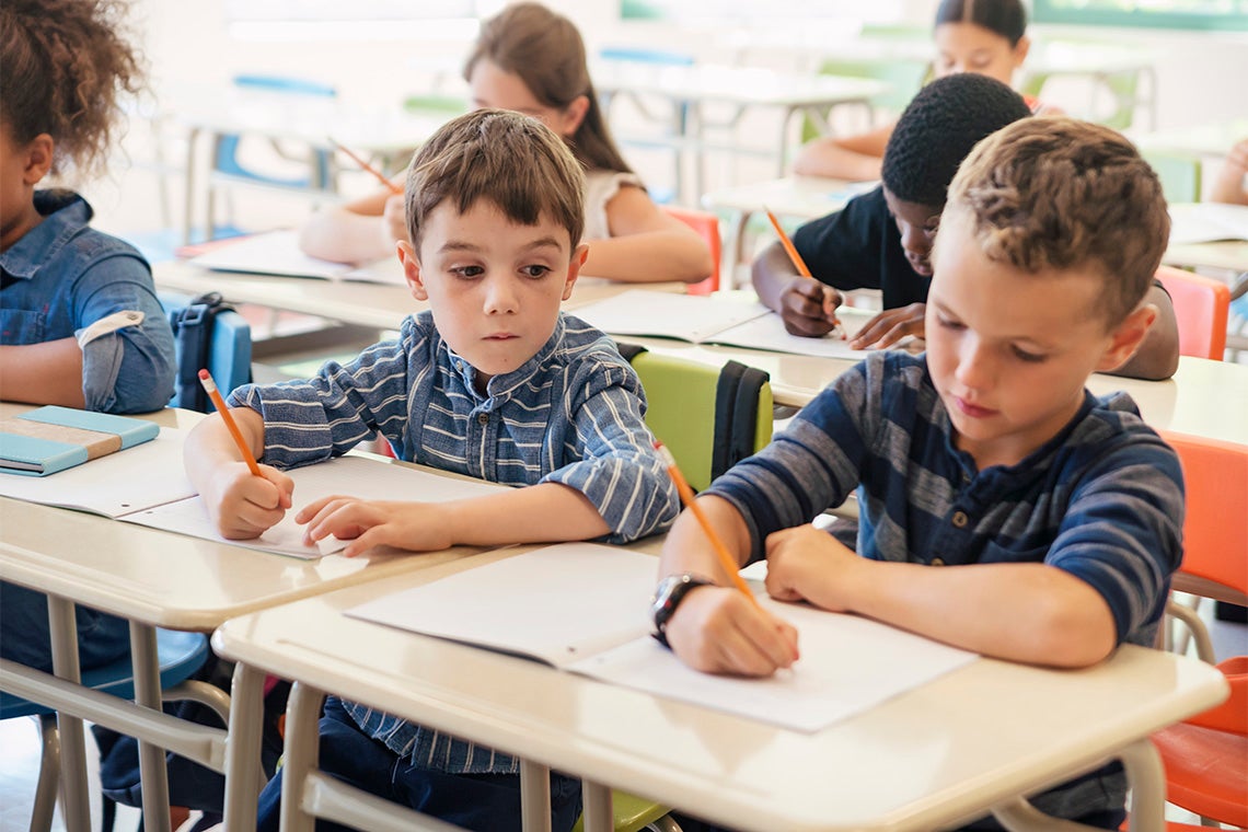 A child peers at another child's work in a classroom