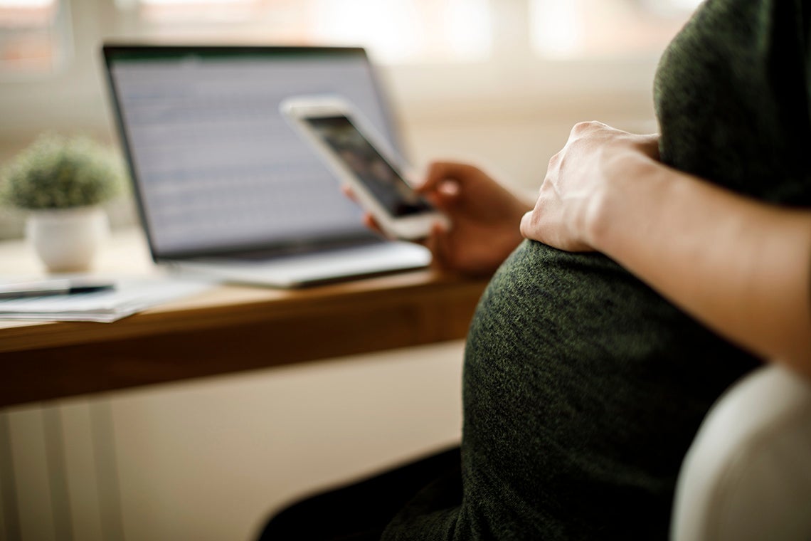 pregnant woman holds her tummy while using a smartphone at a desk