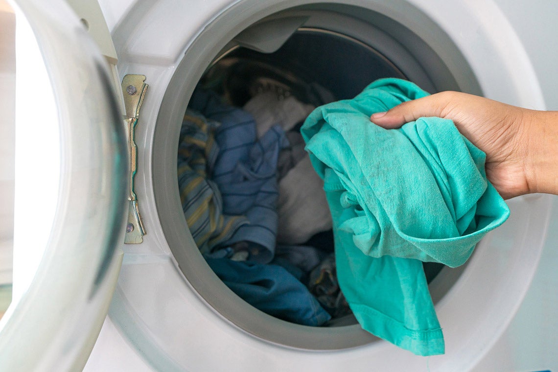 A photo of someone putting clothes into a washing machine