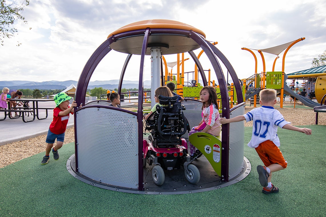children spin an accessible playground structure with children in wheelchairs inside