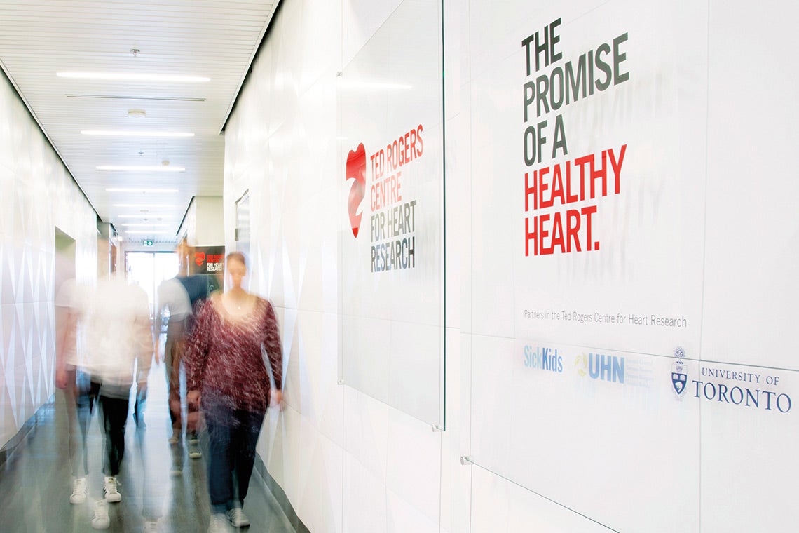 people walking down a corridor at the Ted Rogers Centre for Heart Research. On the wall it reads "The promist of a healthy heart"