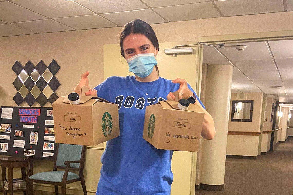 Photo of Vanessa Rezai-Stevens, wearing a blue mask, and holding two cardboard carafes of coffee