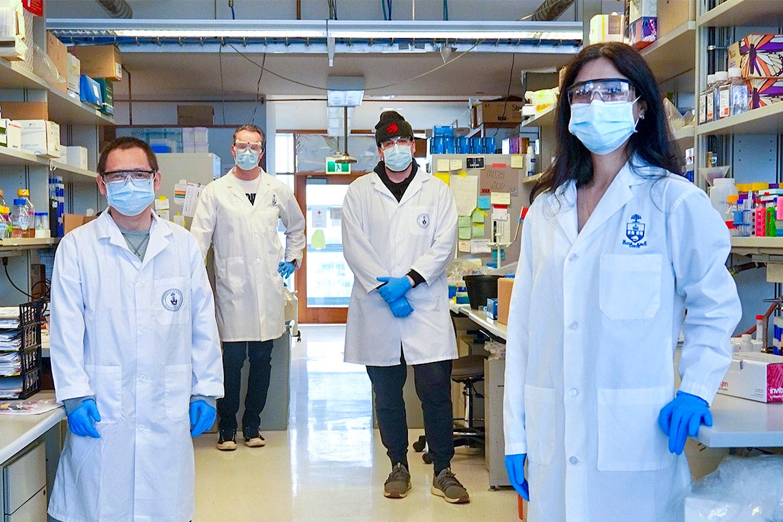 U of T researchers stand two metres apart in a lab, wearing lab coats and masks