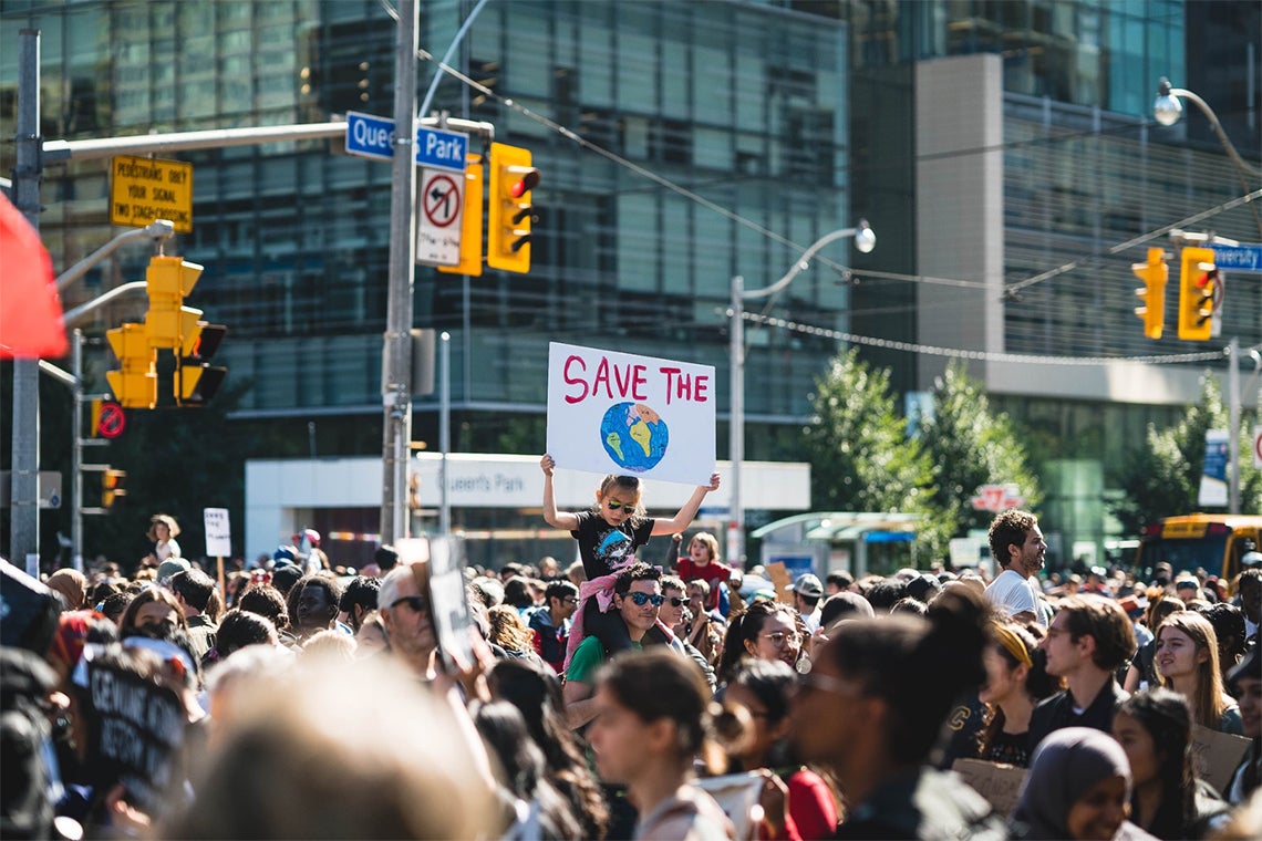 A young girl on her dad's shoulders holds a sign that says "save the earth" during the 2019 Toronto Climate March