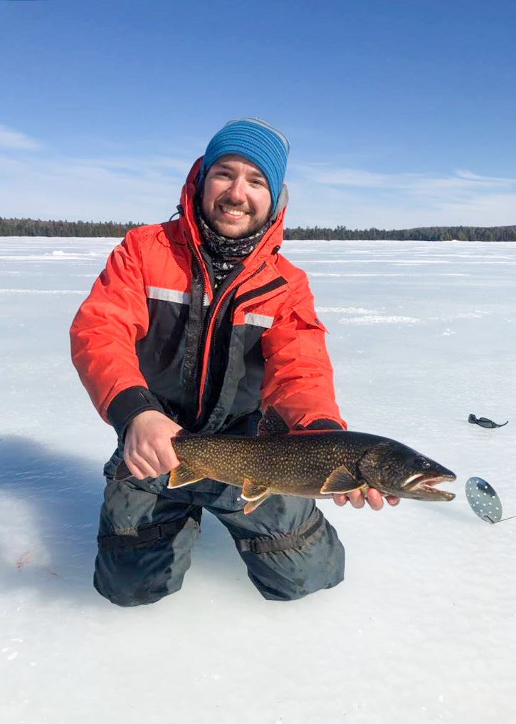 Tim Fernandes holds a lake trout while kneeling on ice