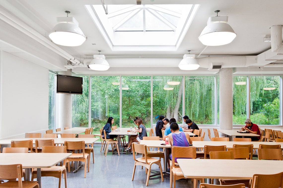 Students eat in a cafeteria at the University of Toronto Mississauga campus with green foliage visible in the background