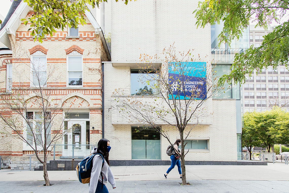 Two students walk past a building at U of T with a sign that says #1 engineering school in canada