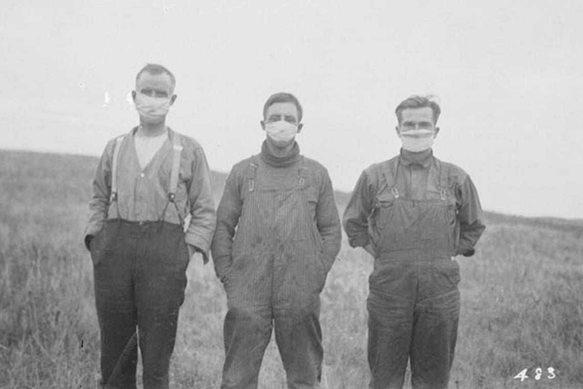 Three men stand in a field in alberta wearing gauze masks