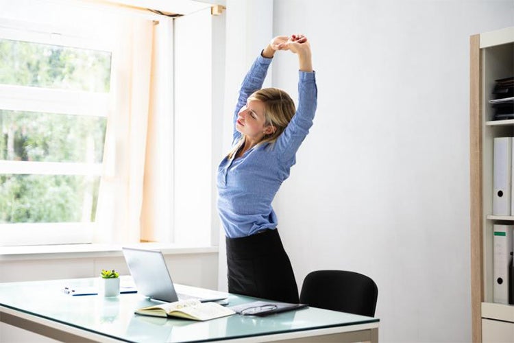 woman stands up and stretches at her desk