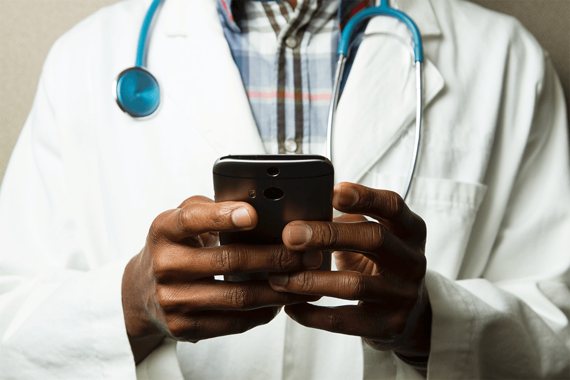 A man wearing a white coat and stethoscope types on a smartphone, representing Hypercare's health-care communications app.