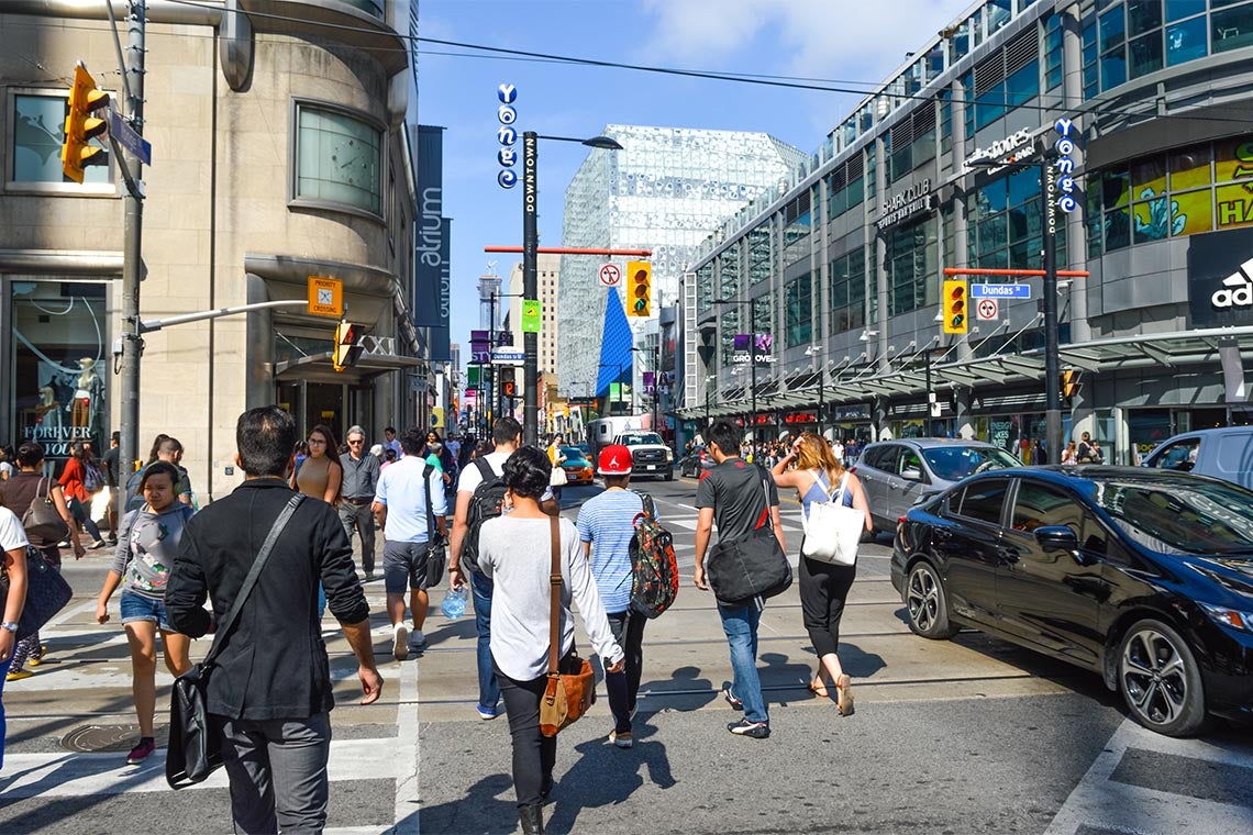 Pedestrians crossing a busy intersection near Dundas Square on Queen Street, in Toronto