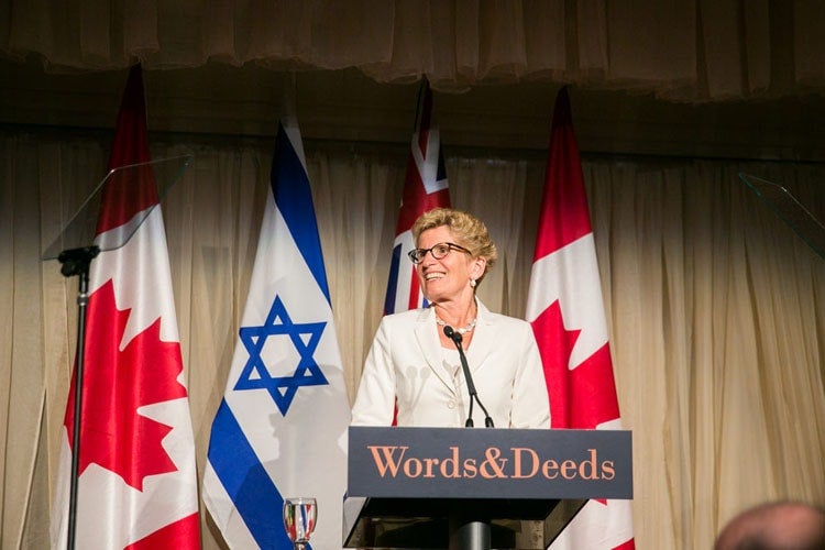 Ontario Premier Kathleen Wynne stands in front of Canadian and Israel flags