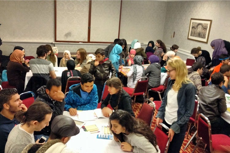 A group of youth working around tables and working together at a workshop