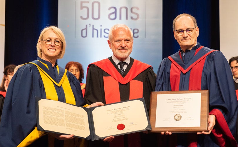 Photo of Professor Normand Labrie holding honorary degree, flanked by University of Quebec at Rimouski's president and rector