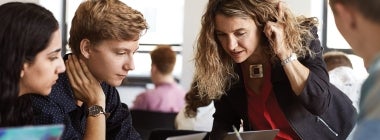 A U of T instructor leans over to help students around a table