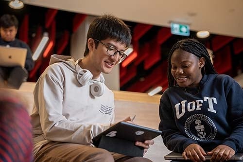 Two U of T students smiling and looking at a tablet