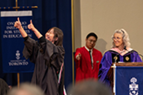 A grad gives two thumbs up to the crowd from the stage