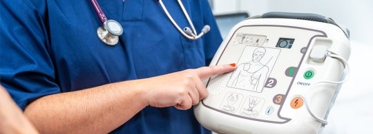 medical doctor hold up a defibrilator and points to the instructions on the unit