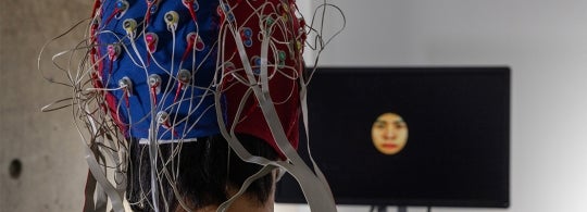 test subject wearing a device on his head while watching a screen with a face on it