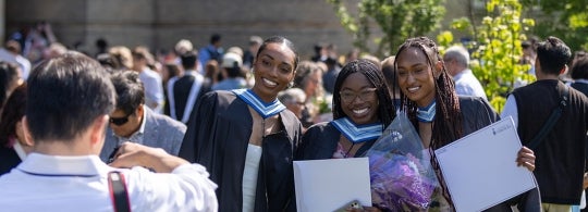 Three grads hold up their degrees while posing for a photo