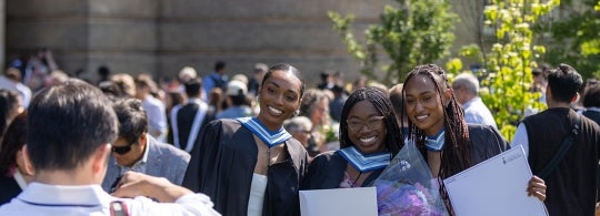 Three grads hold up their degrees while posing for a photo