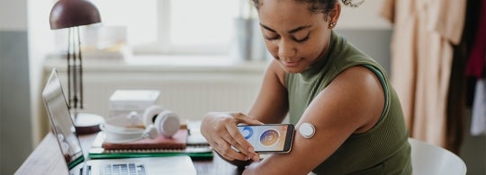 A young woman uses a smartphone to read her glucose monitor on her arm